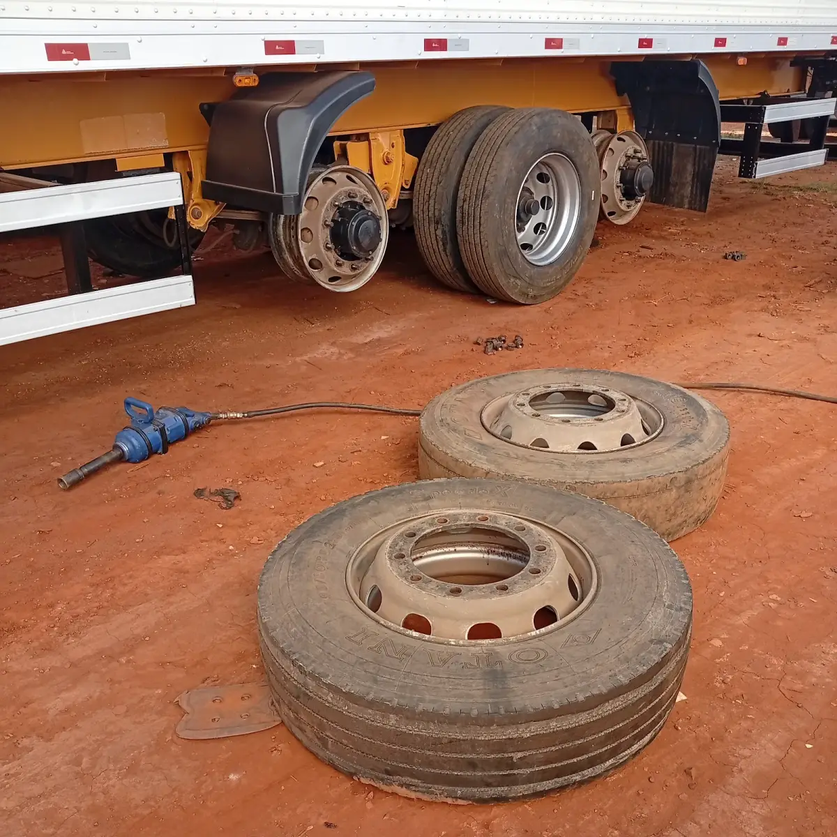duas rodas de carreta tiradas no chão de terra, ao lado da carreta e da chave de impacto